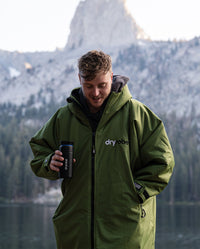 *MALE* stood in front of mountains, holding dryrobe® x Ocean Bottle Brew Flask and wearing Forest Green dryrobe® Advance Long Sleeve