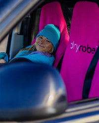 1|Woman wearing Blue dryrobe® Eco Beanie sitting in a car on Pink dryrobe® Water-repellent Car Seat Covers